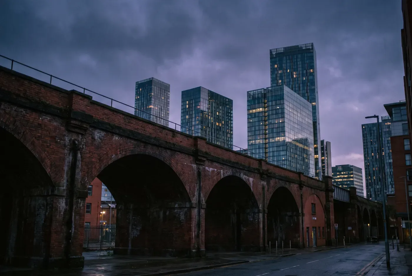 Manchester city centre at dusk, red-brick viaduct and modern Deansgate towers